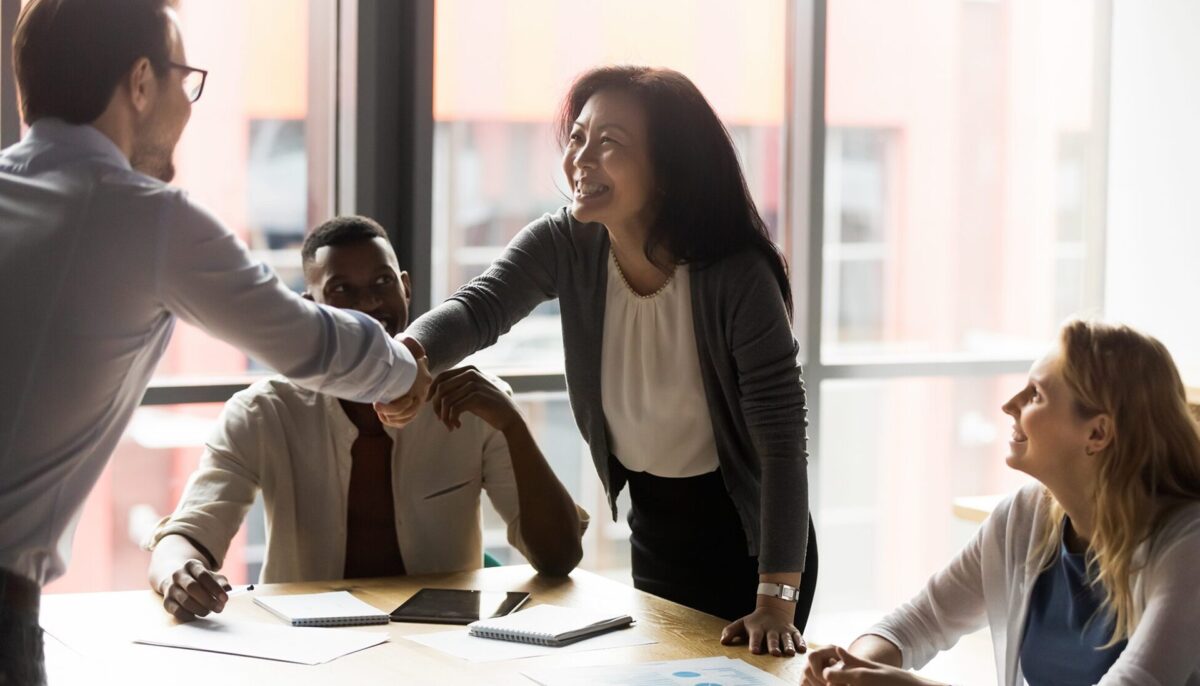 Asian woman shaking hands with a colleague across meeting room table