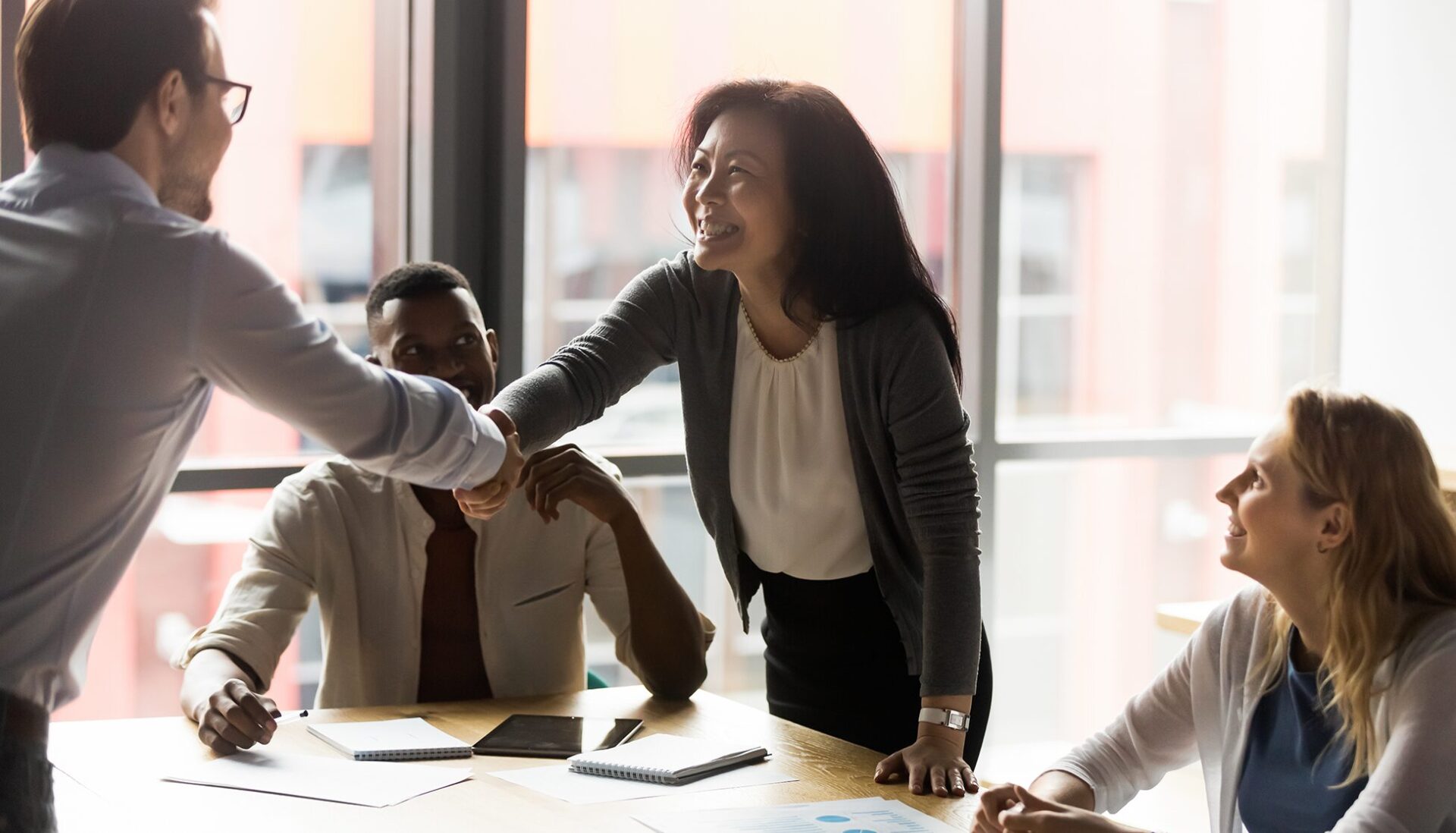 Asian woman shaking hands with a colleague across meeting room table