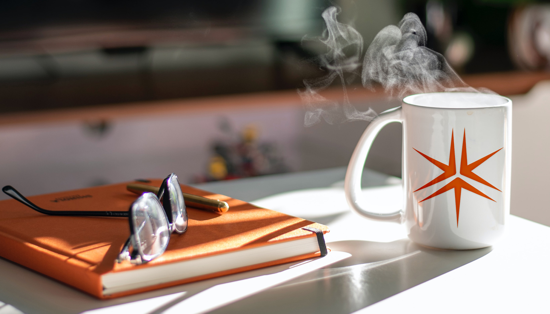 A pair of glasses on an orange, hard-cover book on a counter. Next to it is a white coffee mug emblazoned with the Miller Thomson spark. Steam is emerging from the mug.