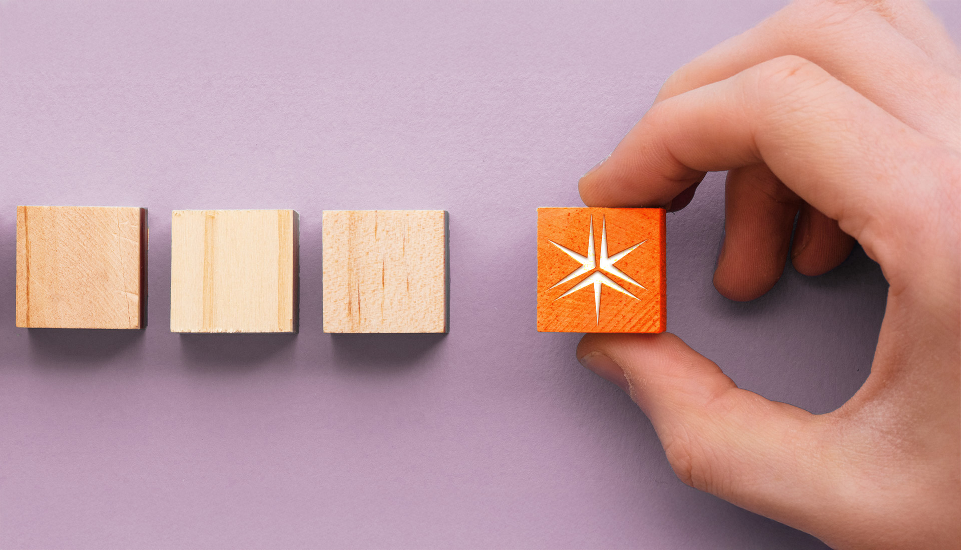 Row of wooden blocks. A hand picks up the last block which features the Miller Thomson spark