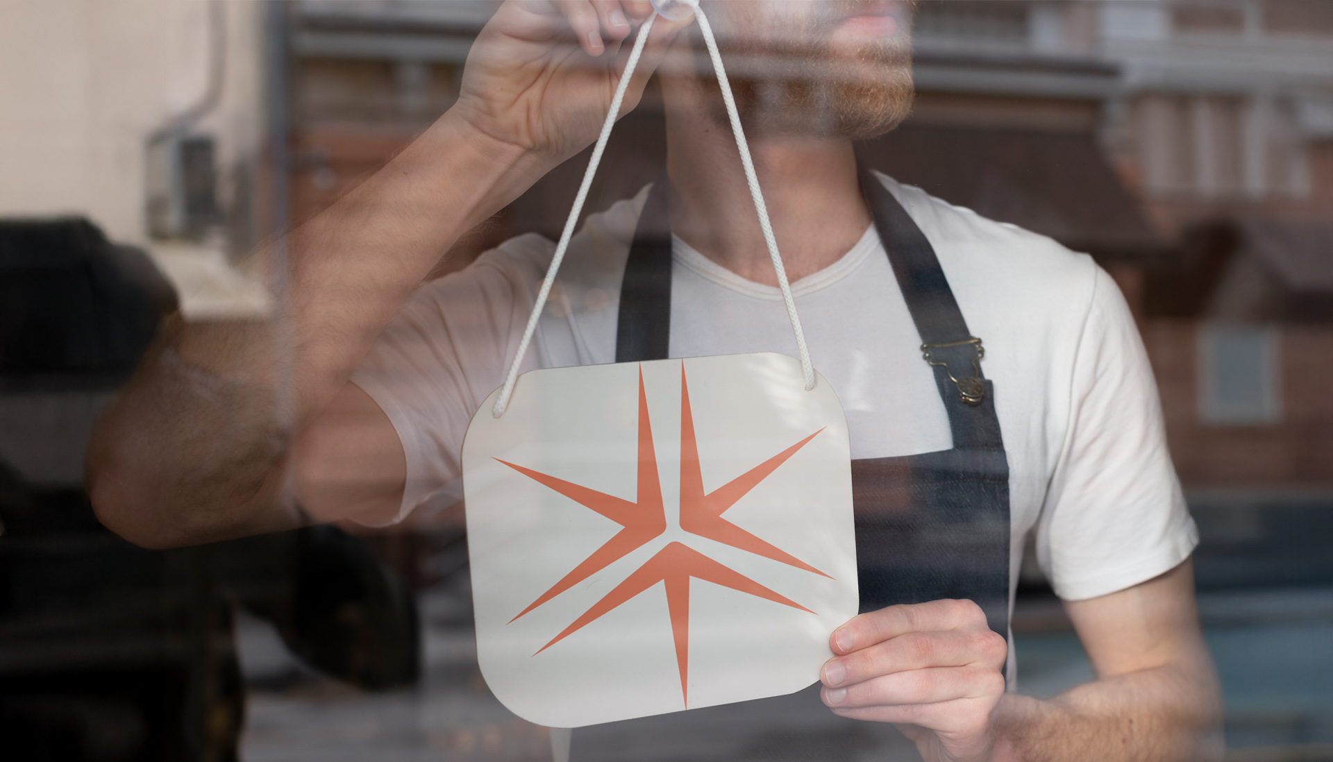 A retail worker wearing an apron puts up a sign in a store window with the Miller Thomson spark