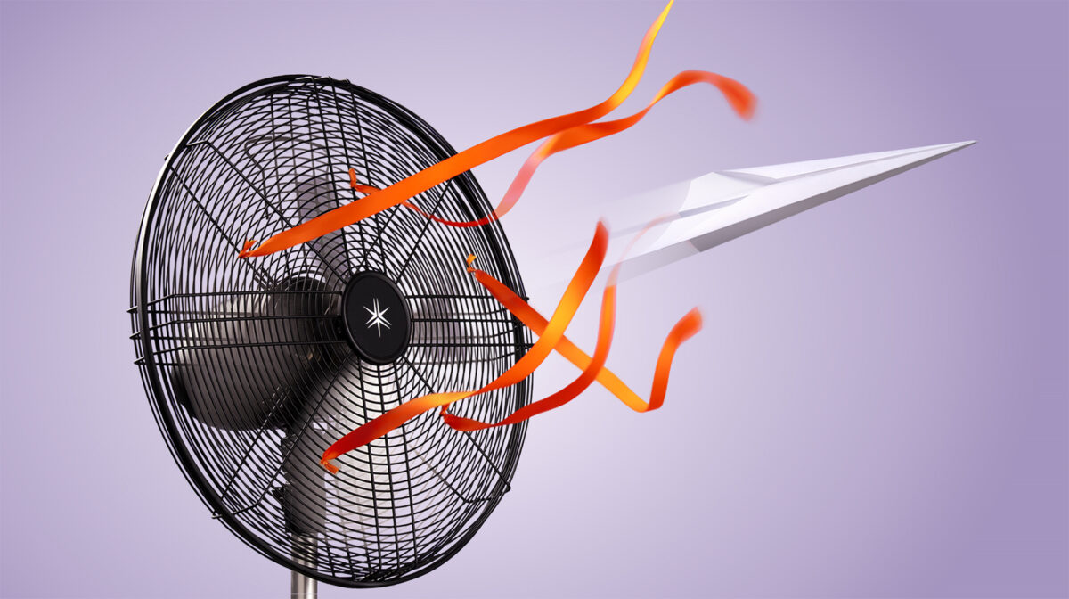 oscillating fan with orange ribbons blowing a paper airplane