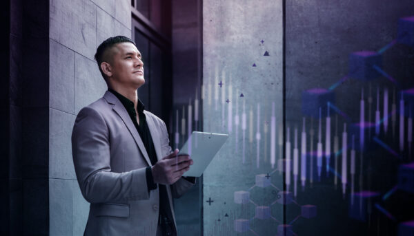 Young man in a suit jacket holding a tablet and standing in front of a office building