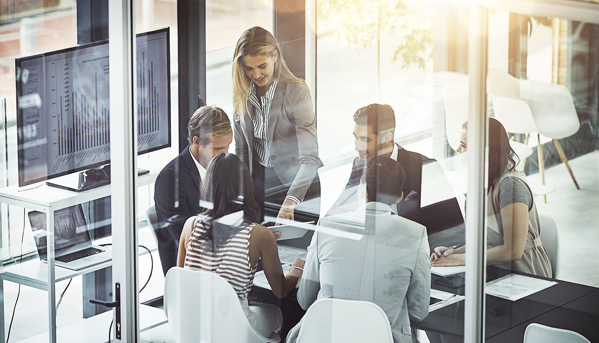 a group of work colleagues in a meeting room with a graph on a tv screen