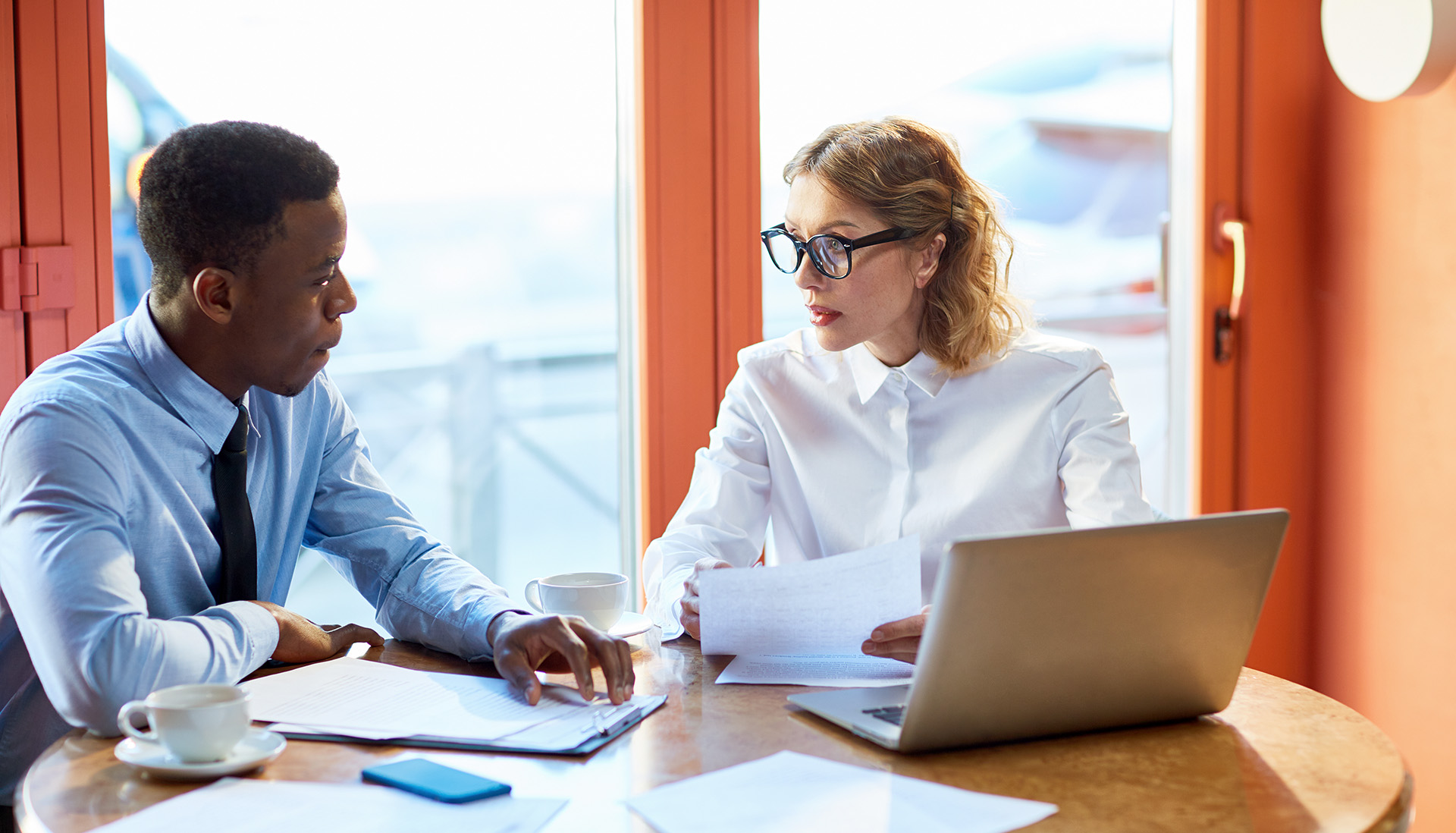 man and woman sitting at a table with documents and an open laptop