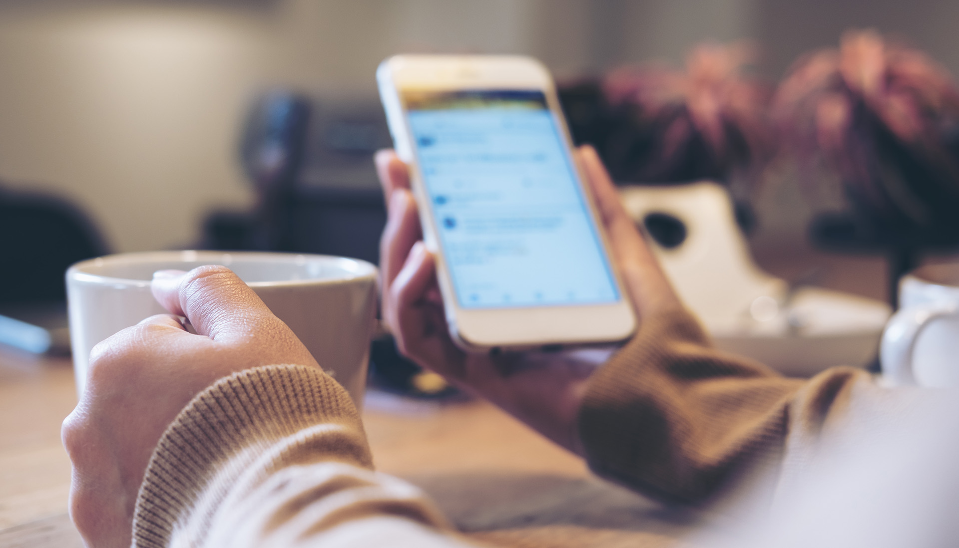 woman scrolling through social media on a smart phone holding a mug of coffee