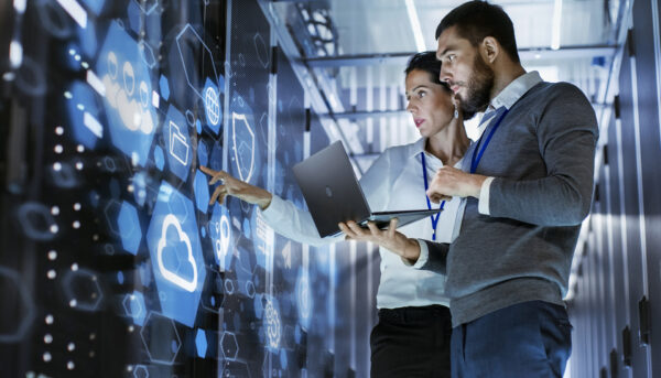 Male IT Specialist Holds Laptop and Discusses Work with Female Server Technician. They're Standing in Data Center, Rack Server Cabinet with Cloud Server Icon and Visualisation.