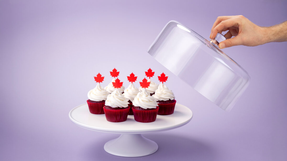 red cupcakes on a cake platter topped with icing and a red maple leaf