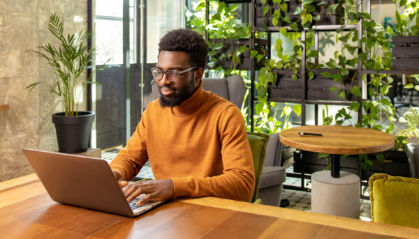 Person working on a laptop at a wooden desk in a modern office filled with natural light and indoor plants.