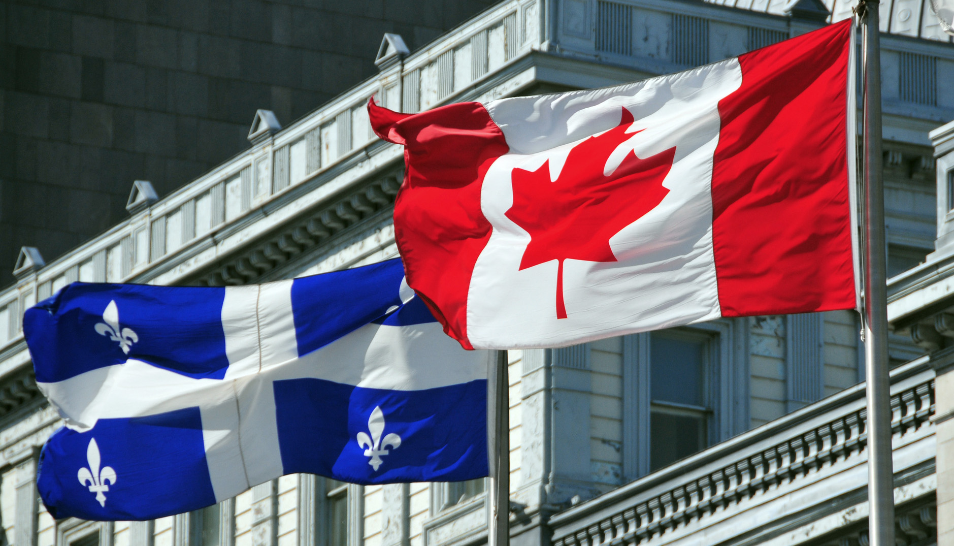 Narrow street in Old Québec lined with historic buildings, storefront signs, and hanging lamps. A flag of Quebec and Canada hang above the street.
