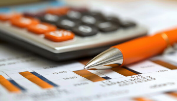 Close-up of an orange pen resting on a printed financial report with charts and data tables, with a calculator blurred in the background