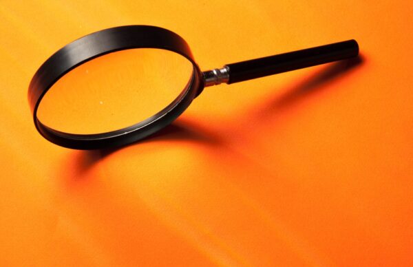Close-up of a black magnifying glass resting on a bright orange surface, with the lens and handle extending diagonally across the image.